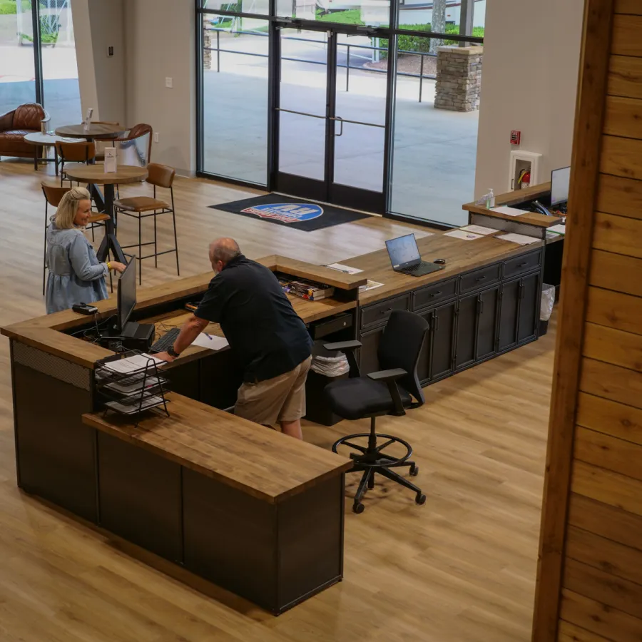 Modern office reception area with wooden desks, two people conversing, and large glass doors in background