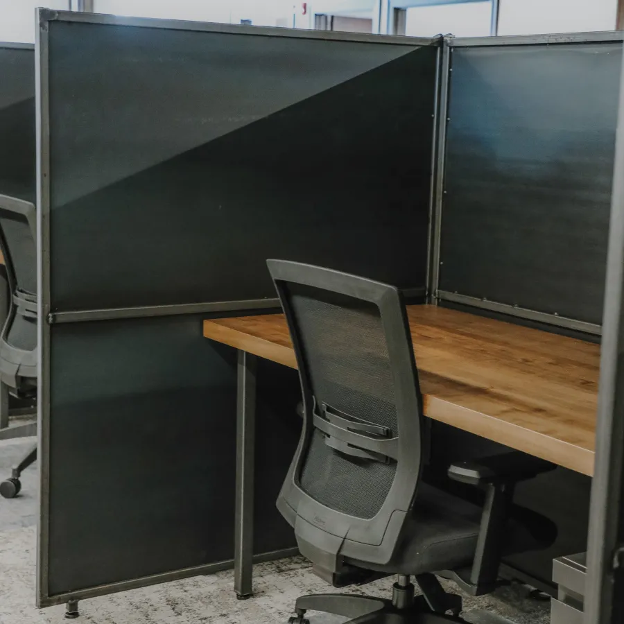 Empty modern office cubicle with wooden desk and black mesh ergonomic chair under natural light