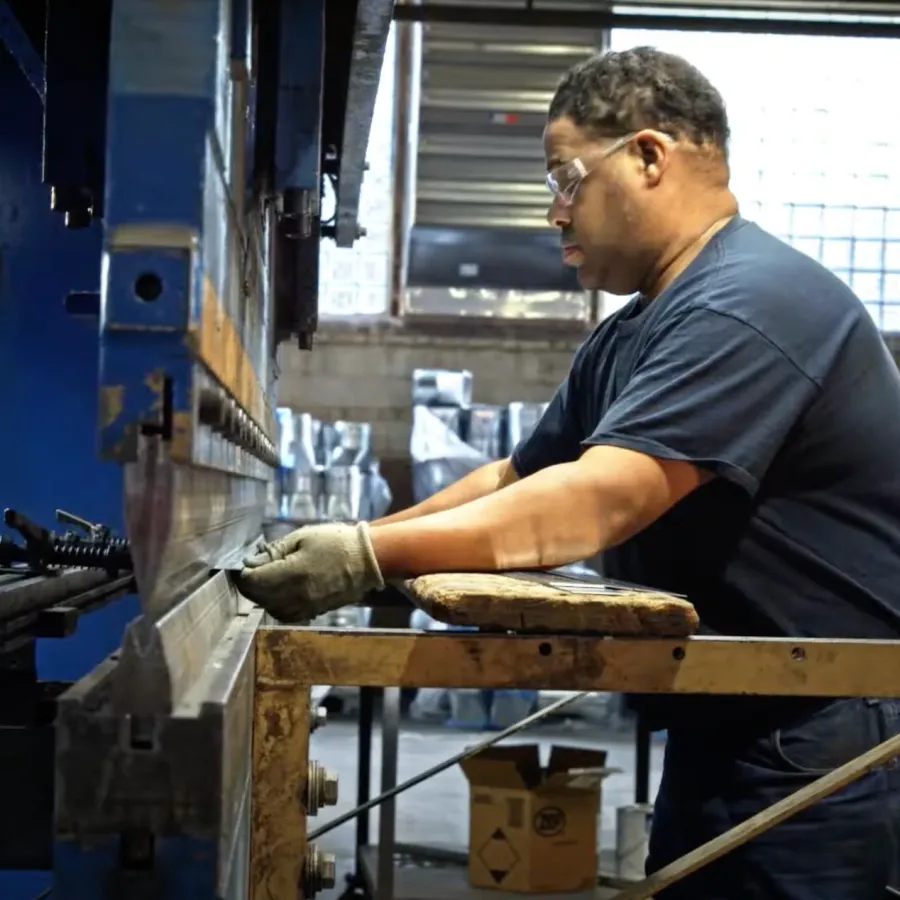 Worker operating industrial metal press machine in factory setting with safety goggles and gloves