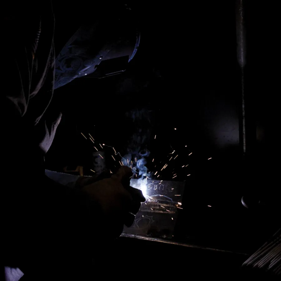 Welder working with sparks and bright light in a dark workshop, wearing protective gear.