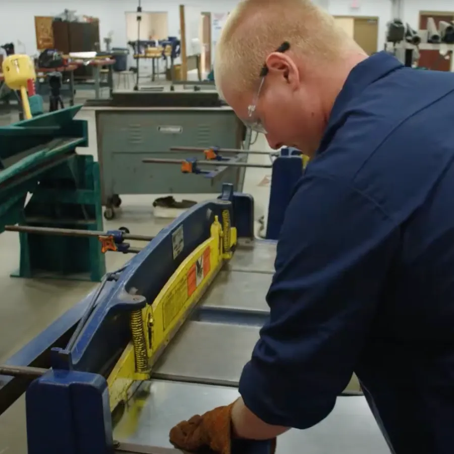 Worker using industrial cutting machine in a workshop with safety gear and equipment around.