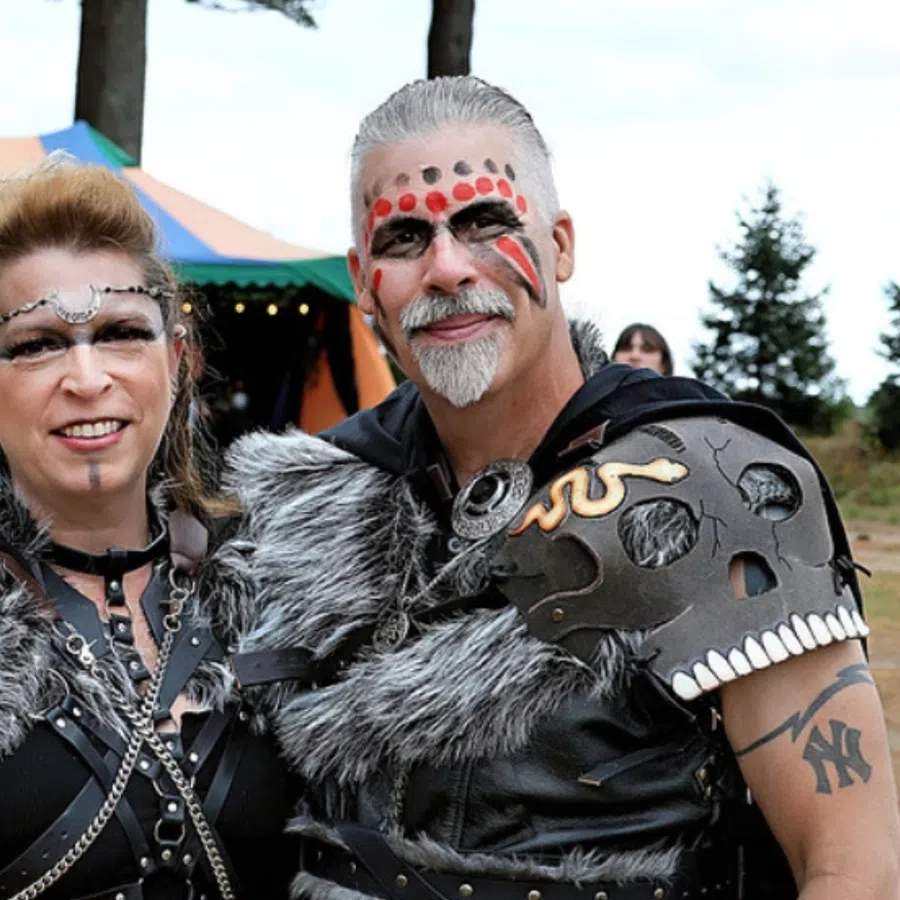 A man and woman dressed in Viking-inspired costumes with face paint and a colorful tent in the background at an outdoor event.