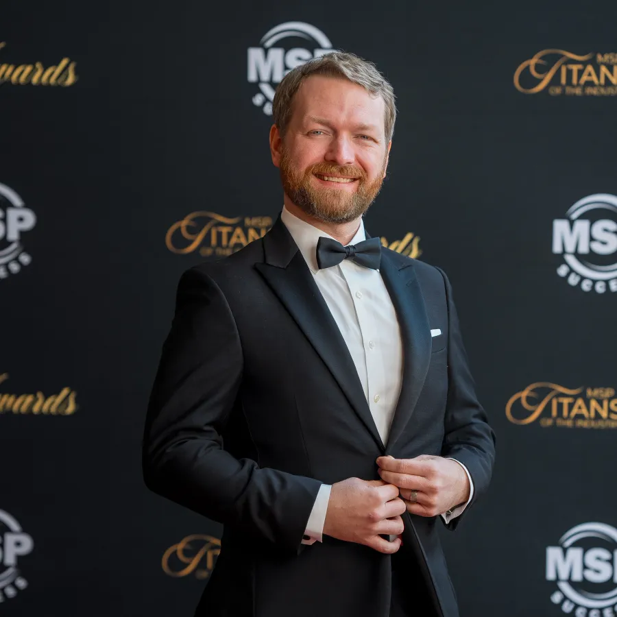 a man in a suit and bow tie standing in front of a large gold and black banner