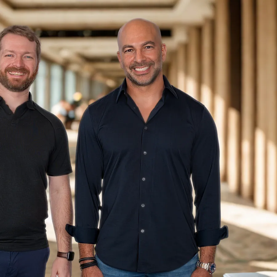 Two men standing and smiling in a bright hallway with large windows and pillars in the background