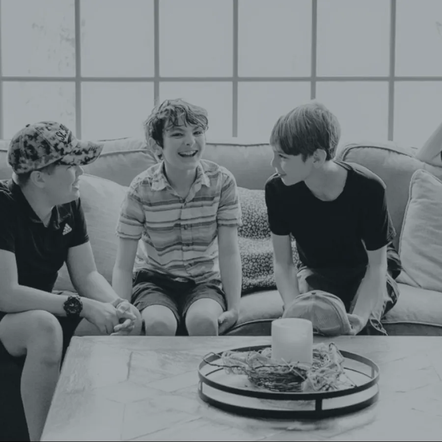 Four boys sitting and chatting on a couch in a bright living room with a coffee table in front of them