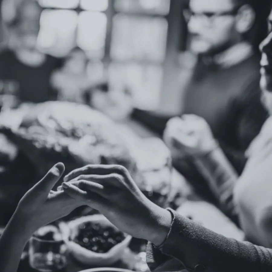 Black and white image of two people holding hands with blurred background at a social gathering.