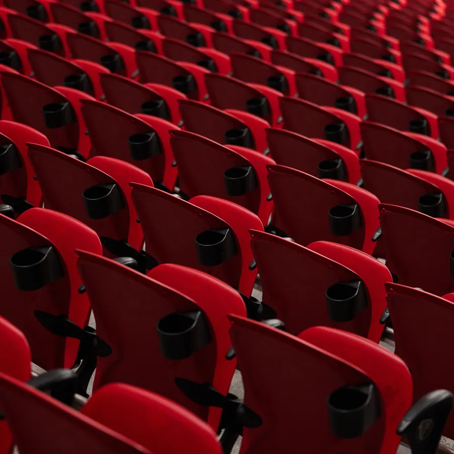 Rows of empty red stadium seats with black cup holders arranged in a pattern under soft lighting.