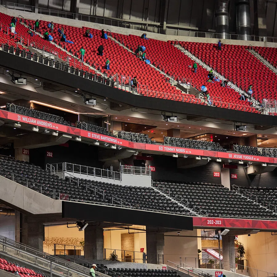 Workers clean empty red and black stadium seats inside a modern sports arena under artificial lighting.