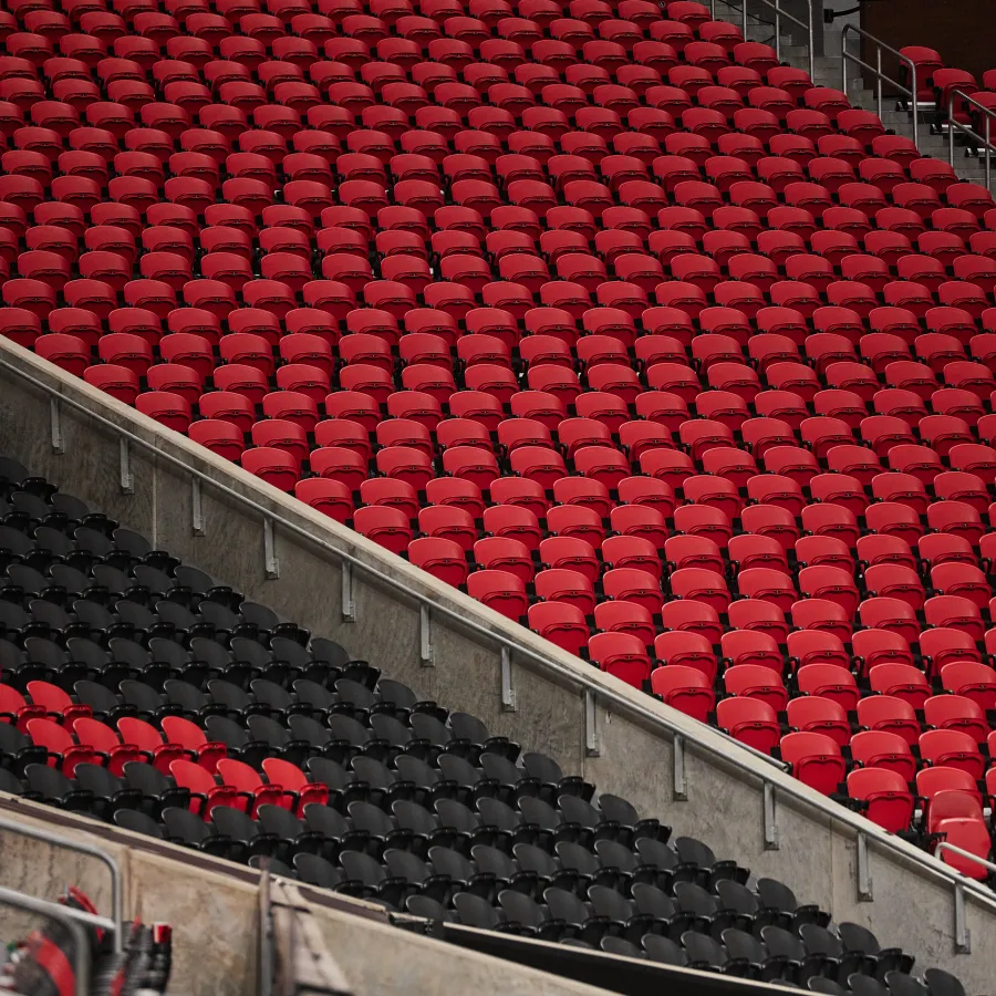 Rows of empty red and black stadium seats in a geometric pattern with concrete steps and metal railings.