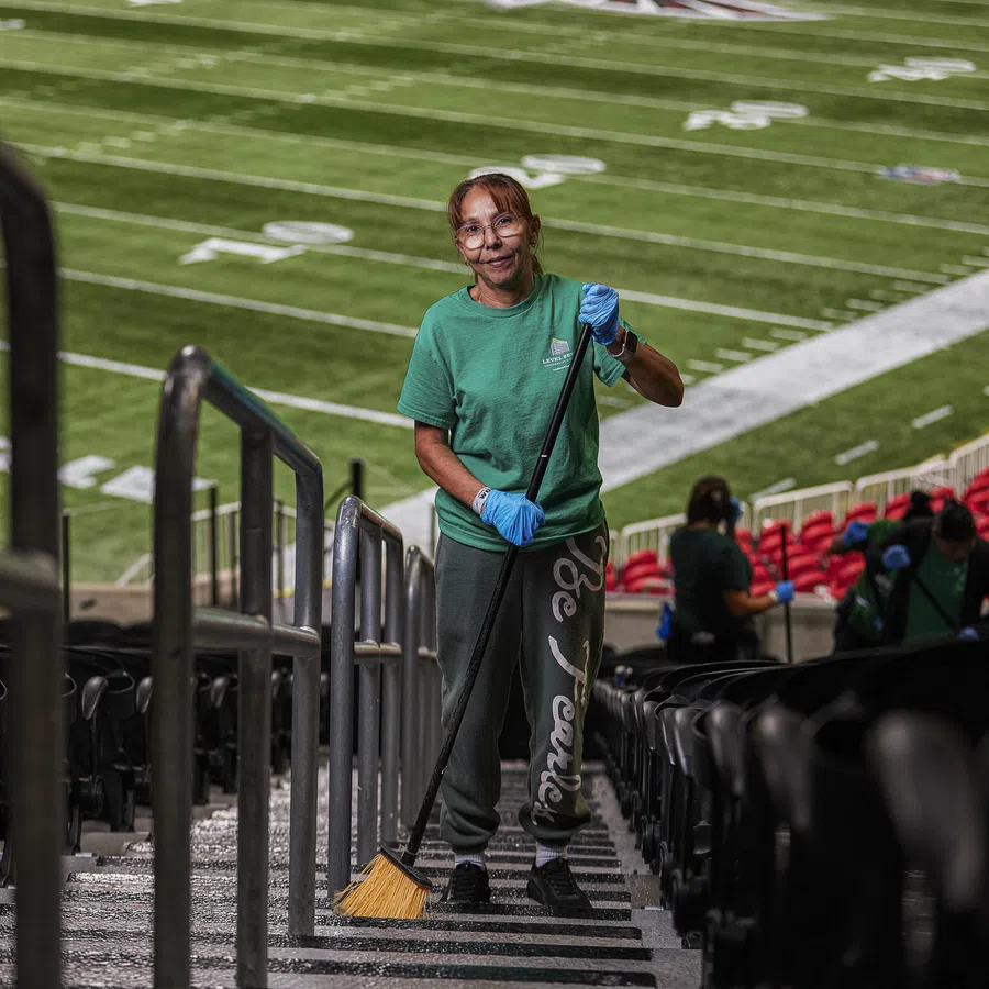 Stadium worker sweeping stairs in empty football stadium with green field and red seats in background
