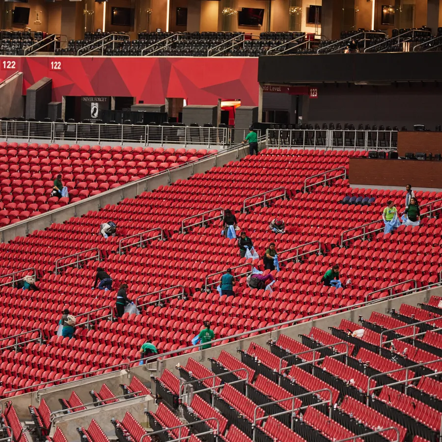 Workers cleaning and disinfecting rows of empty red stadium seats before an event starts.