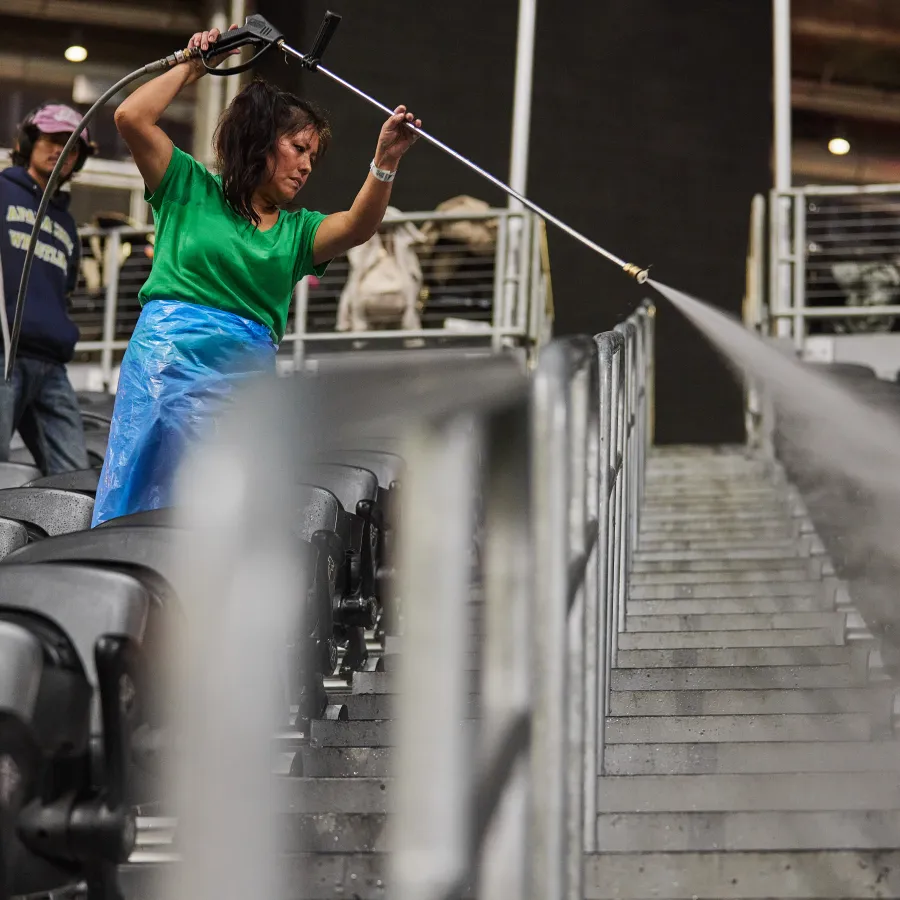 Woman pressure washing seats and aisle steps in an empty stadium or arena before an event begins