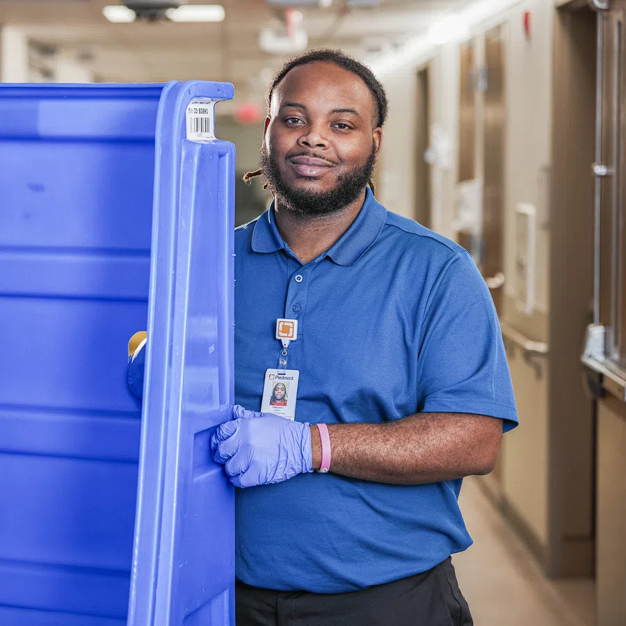 Warehouse worker wearing blue uniform and gloves handling large blue plastic containers in a hallway