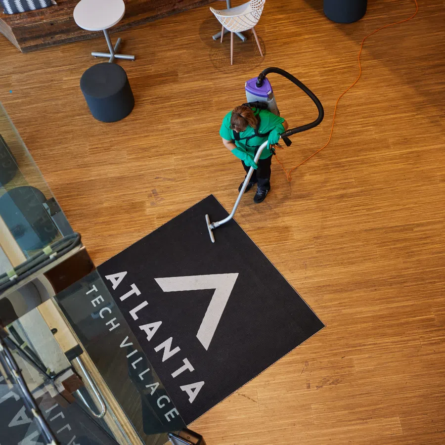Person cleaning a black Atlanta Tech Village floor mat on wooden floor in modern office lobby