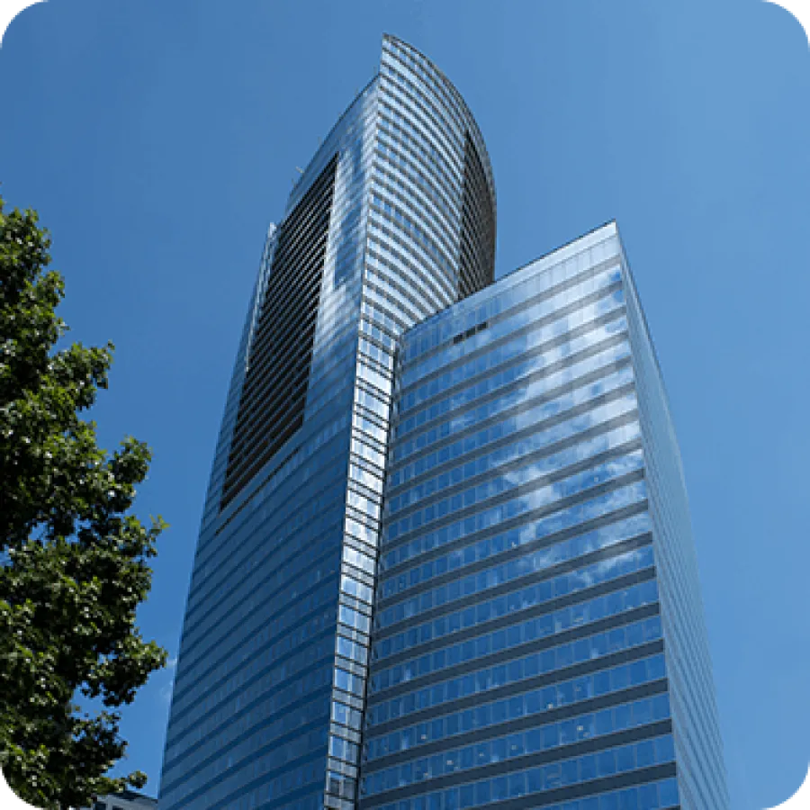 Modern glass skyscraper reflecting blue sky and clouds with green tree on the side