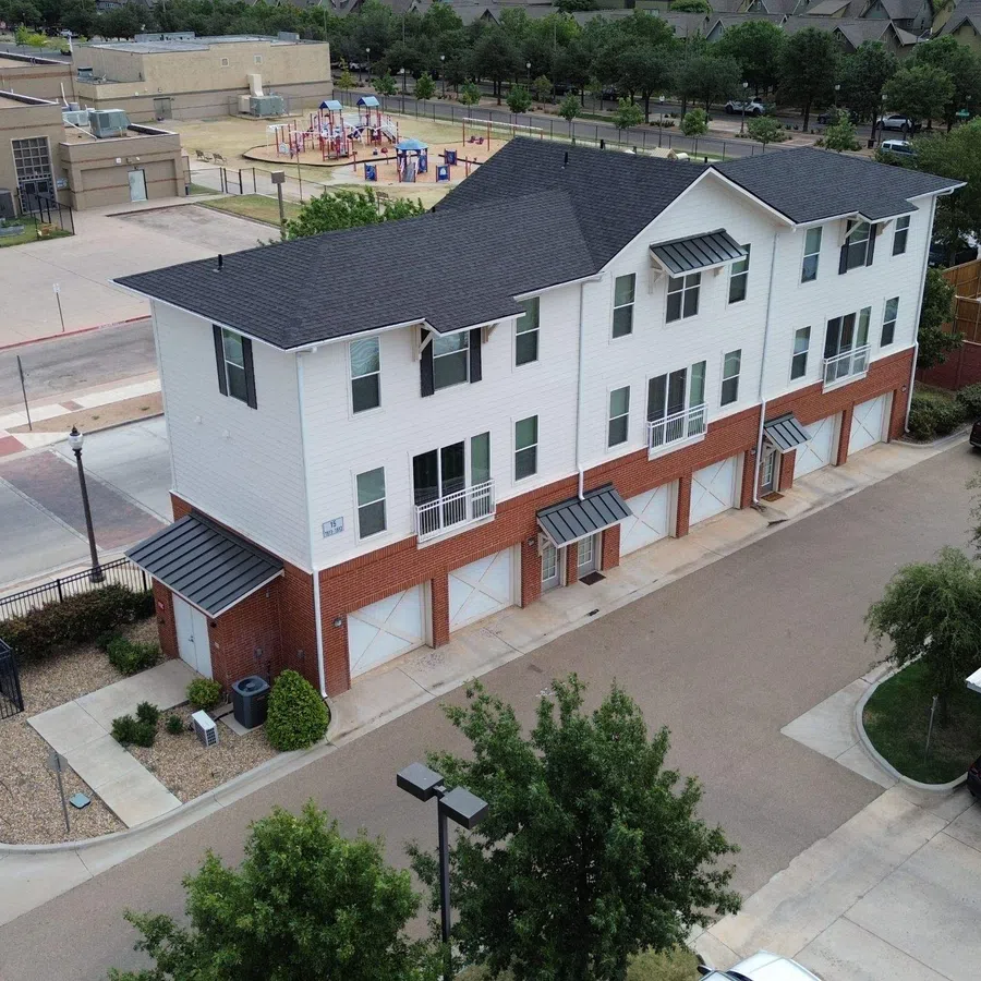 Aerial view of a completed multi-family apartment complex reroof in Lubbock, Texas, featuring new charcoal architectural shingle roofing across multiple three-story residential buildings with parking areas in the foreground.
