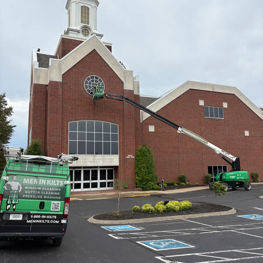 Men in Kilts cleaning windows on a church using a green lift and van in a parking lot with handicap spaces.