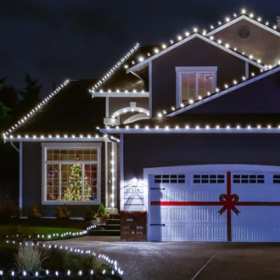 House decorated with white Christmas lights and a garage door wrapped like a gift with a red ribbon at night.