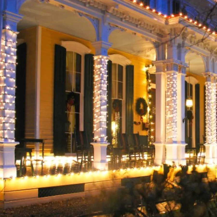 Victorian house porch decorated with festive white string lights and wreaths in the evening.