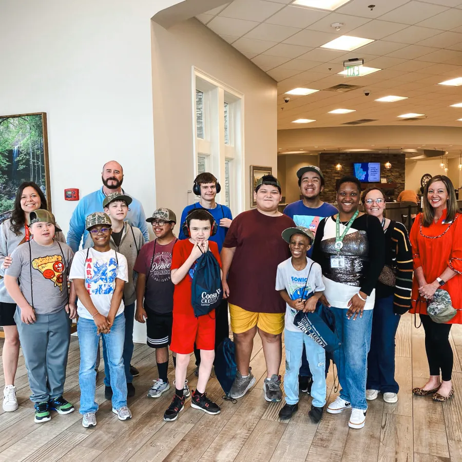 Group of diverse children and adults smiling indoors in bright room with wooden floors and benches.