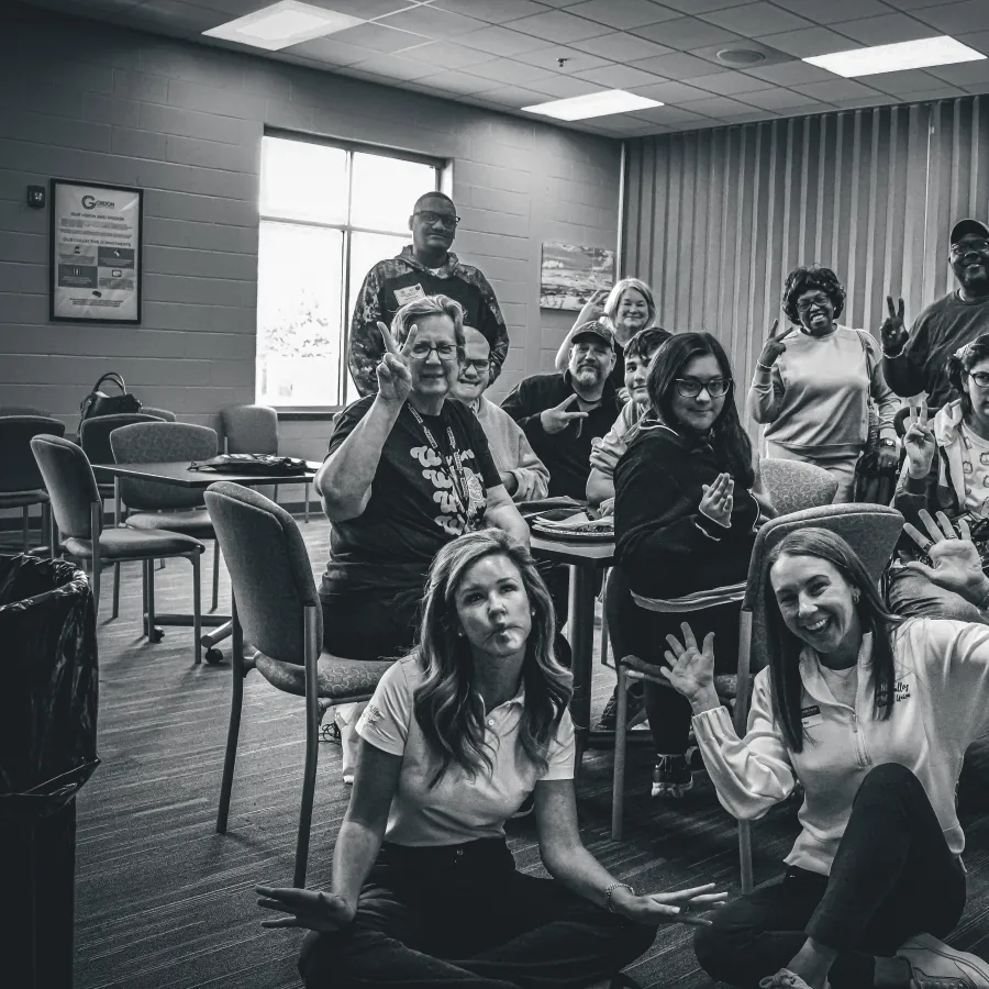 Black and white group photo of diverse people in a room smiling and making hand gestures, seated and standing.