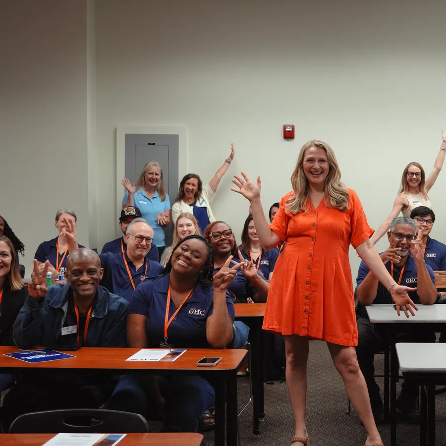 Smiling group of diverse students and teacher in orange dress posing happily in classroom with raised hands.