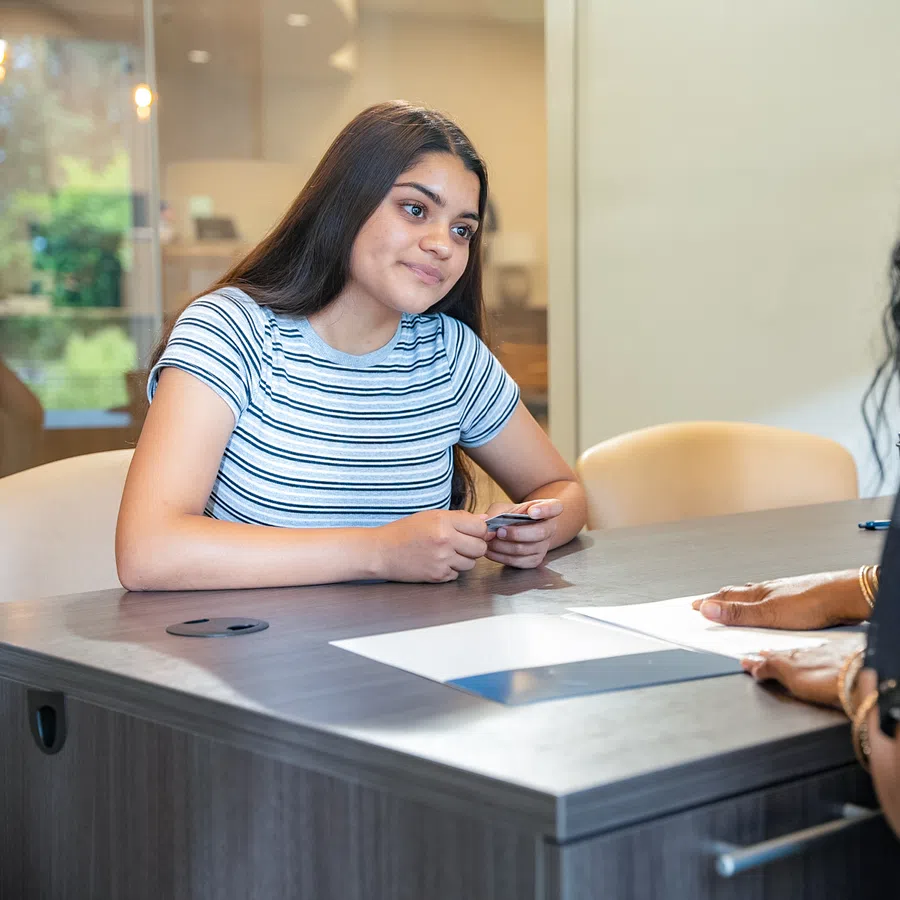 Young woman in striped shirt attentively listening during a meeting across a table with another person.