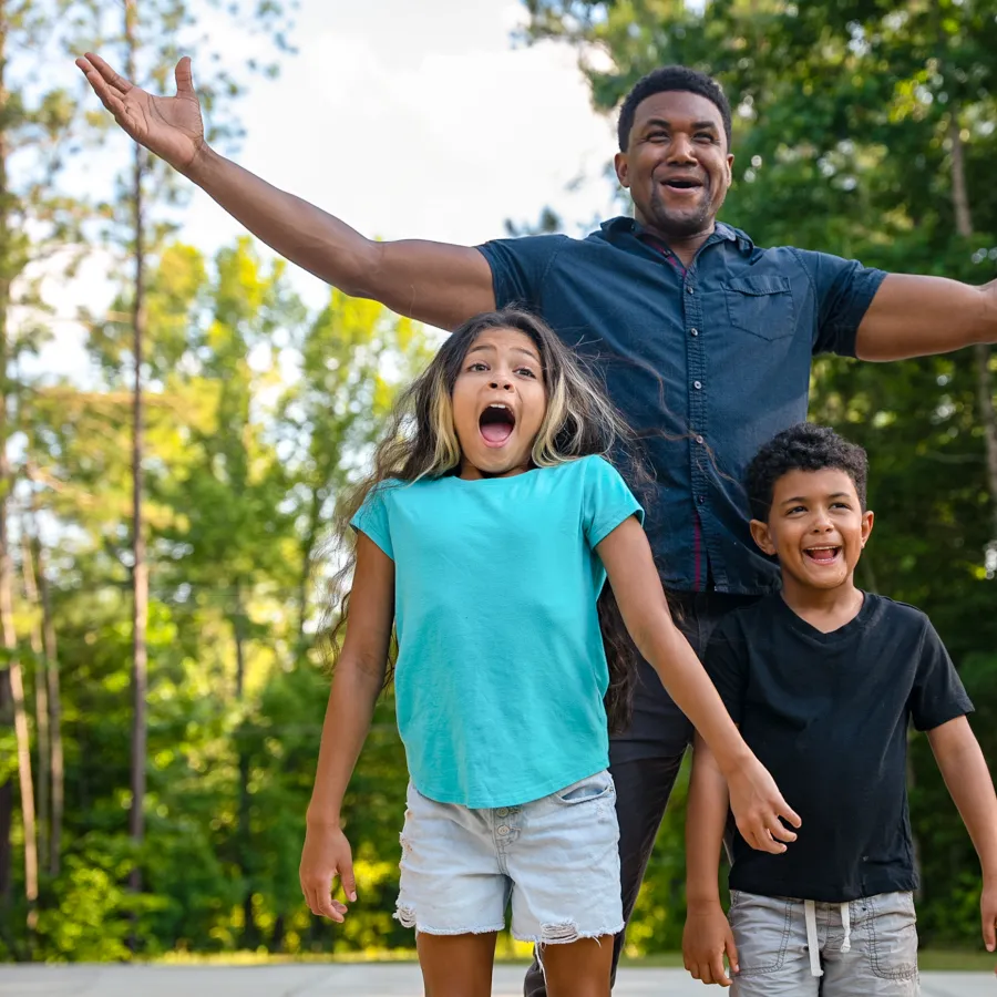 Happy man with two excited children outdoors surrounded by trees on a sunny day