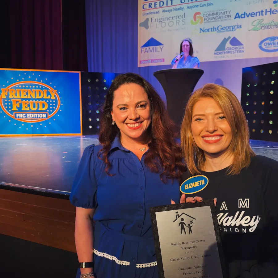 Two smiling women holding an award at a Friendly Feud FRC Edition event with sponsor logos projected behind them.