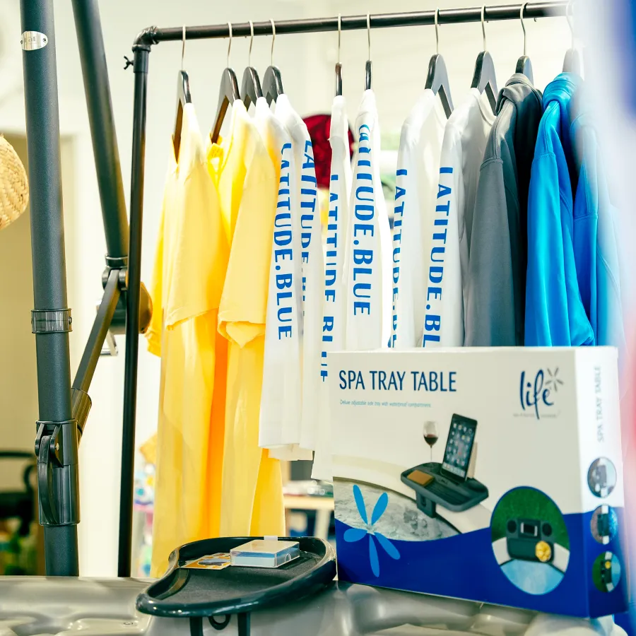 Colorful t-shirts hanging on rack with a boxed spa tray table and a straw hat in a bright indoor setting