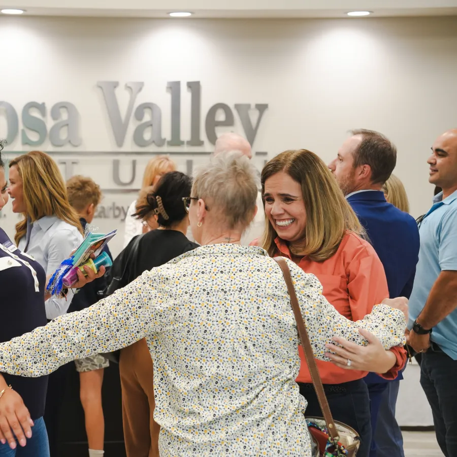 People warmly greeting and embracing each other in a lively Coosa Valley Credit Union event lobby.