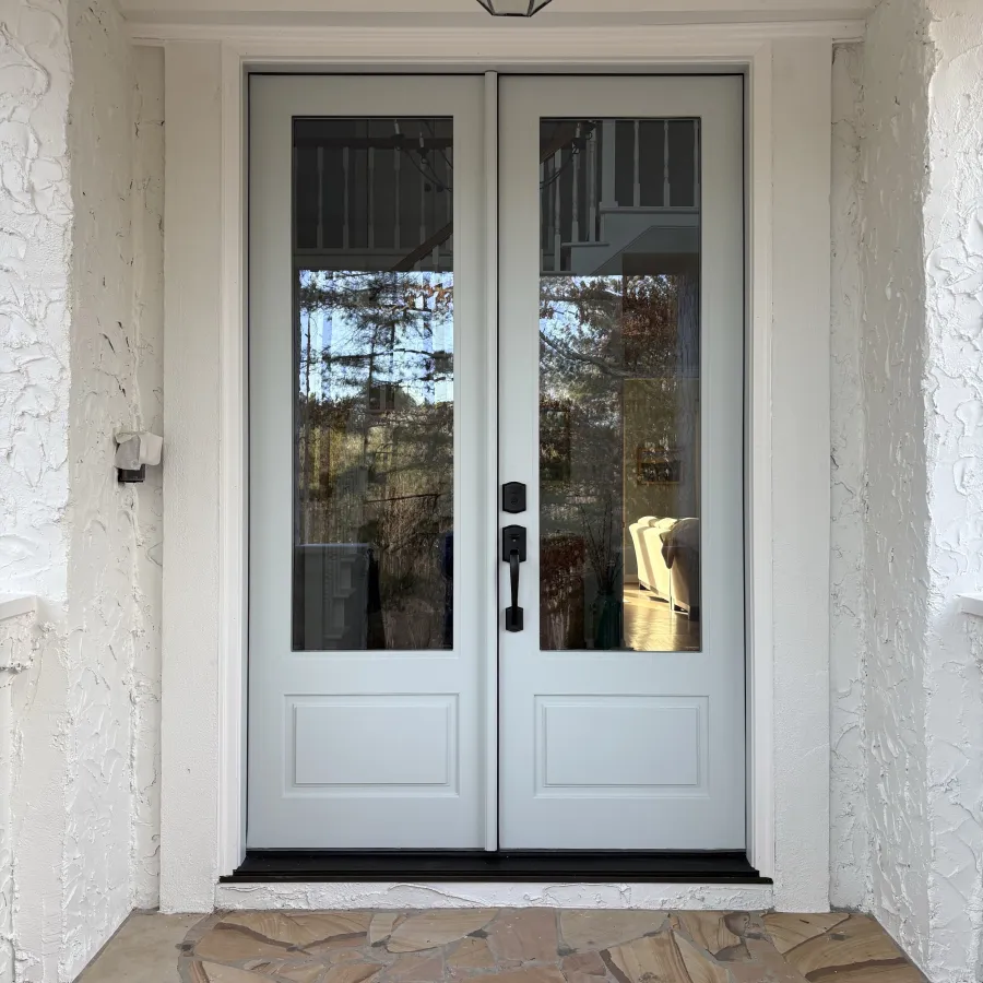 Light blue fiberglass double front door with glass panels, black handles, stone tiled porch, and overhead exterior light fixture.
