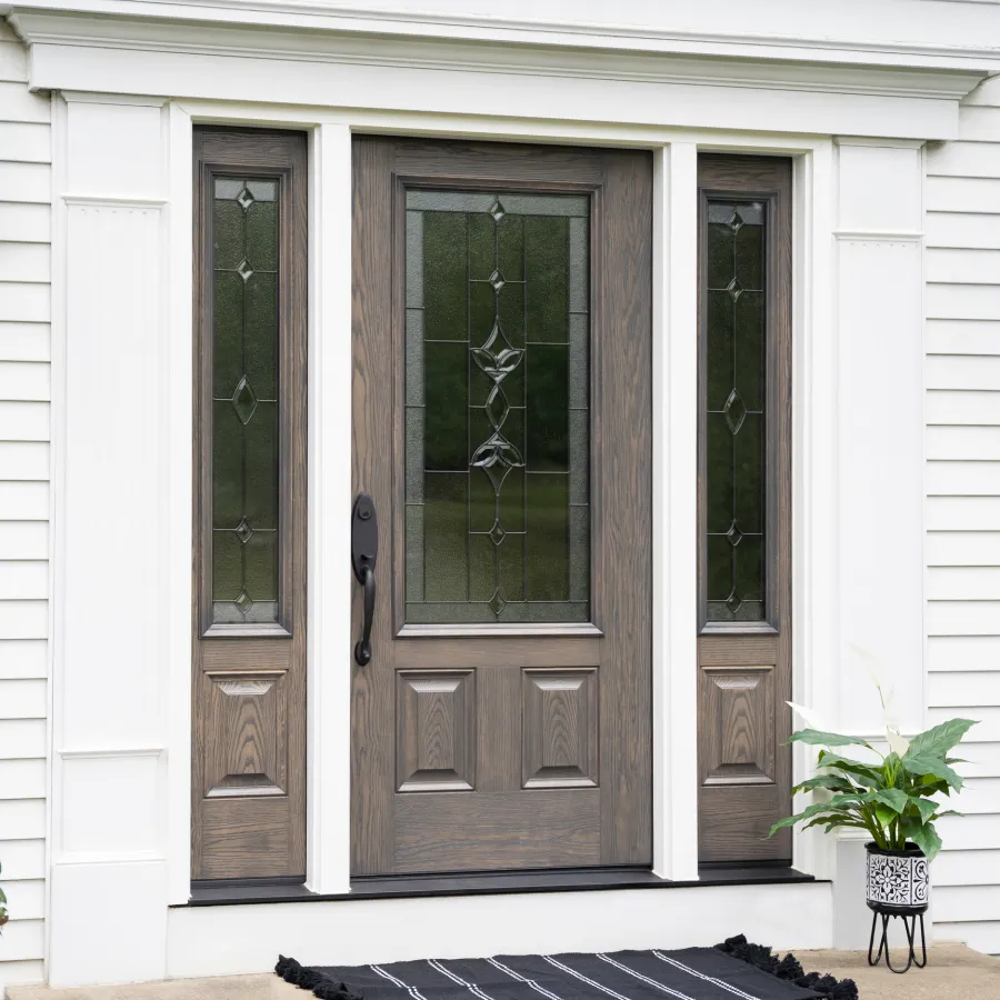 Front door with decorative glass panels on a white house exterior with siding and a potted plant.