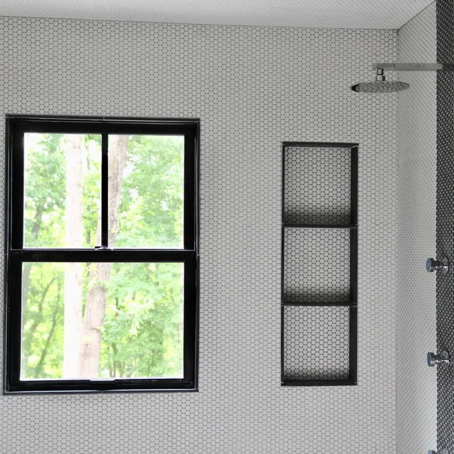 A white and black penny tiled shower with a black double hung fiberglass window on the shower wall