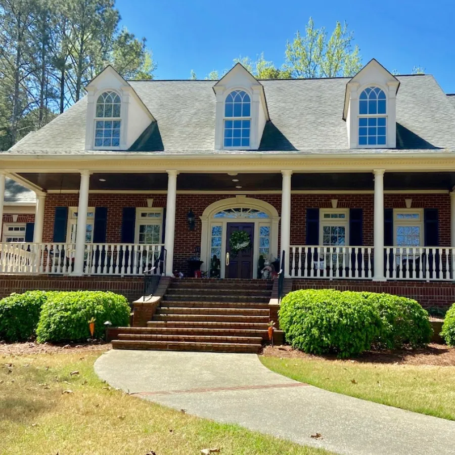 Brick house with large porch, white railings, arched windows, and stairs leading to a brown front door with wreath.