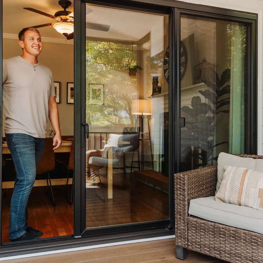 A young man walking out a black sliding glass door onto a balcony