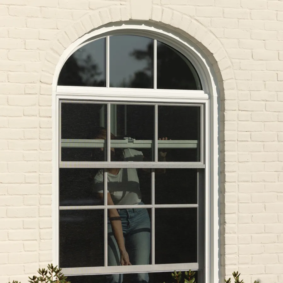 A person opening a double hung round top window on a white brick house