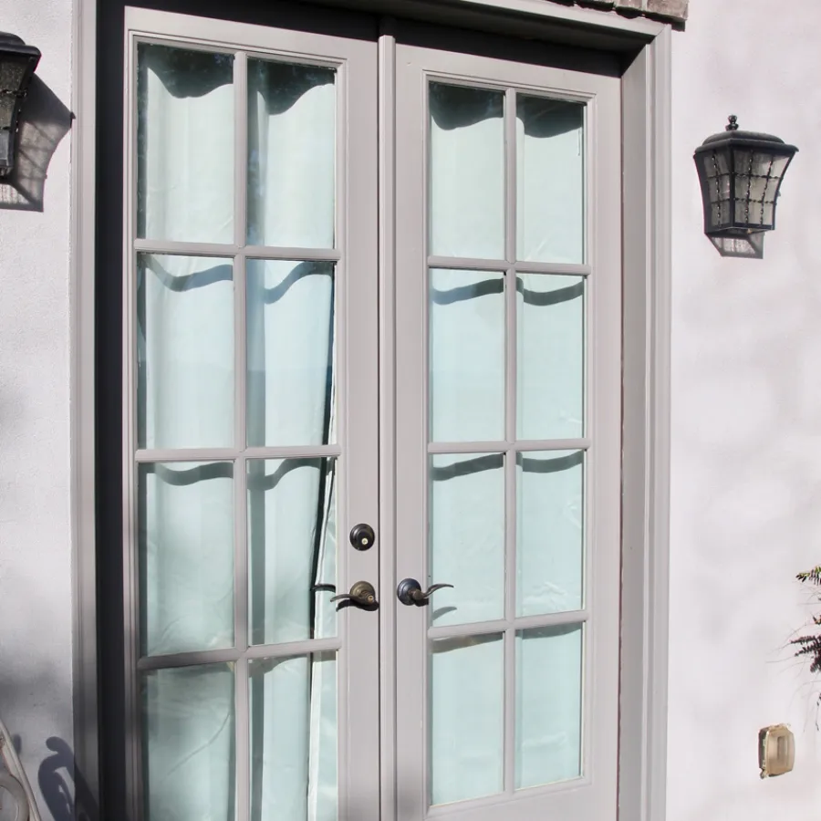 Gray French doors with multiple glass panels, light blue curtains, and outdoor wall lanterns beside them.