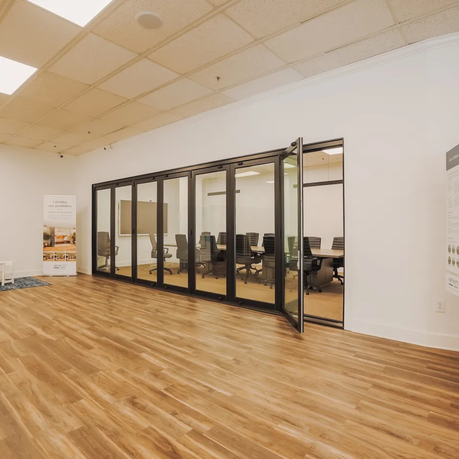 Spacious office area with wooden flooring and a glass-wall conference room featuring black chairs and a large TV.