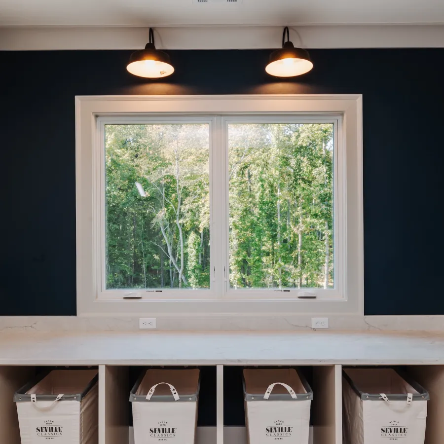 Modern kitchen with dark blue walls, white cabinets, marble countertops, and a large window showing green trees outside.