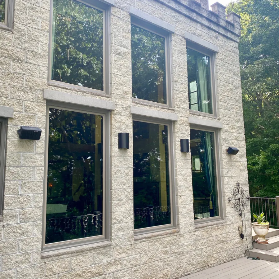 Stone exterior wall with tall windows reflecting trees and black wall lights on a wooden deck patio.