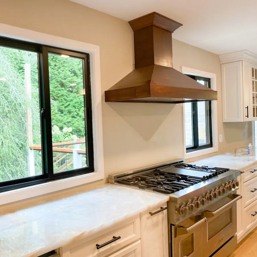 a kitchen with a stove and chimney with black slider windows on either side of the stove
