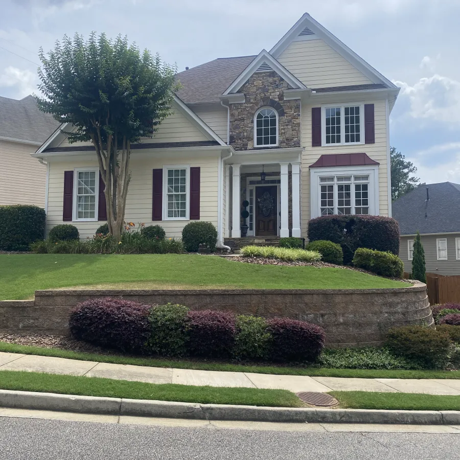 Charming two-story house with stone accents and beautifully landscaped yard on a sunny day.