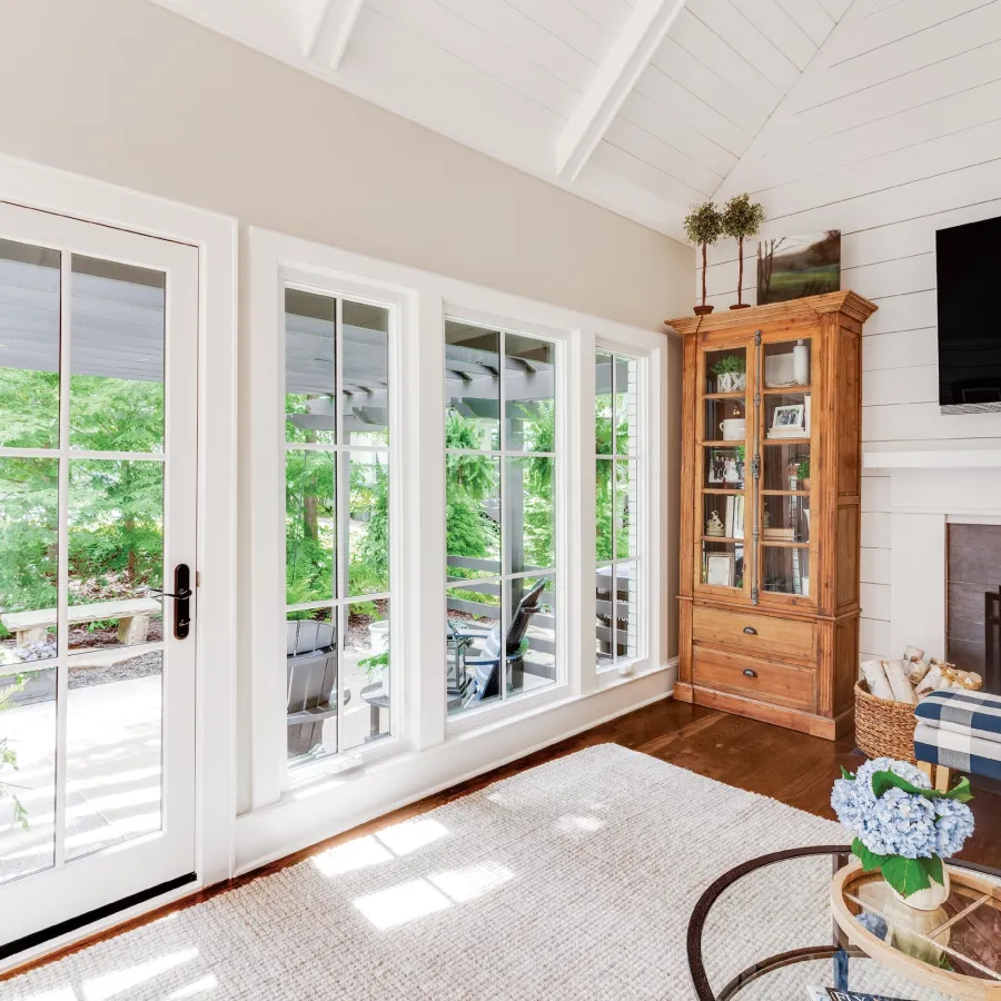 White framed glass patio door next to white casement windows overlooking backyard from living room. 