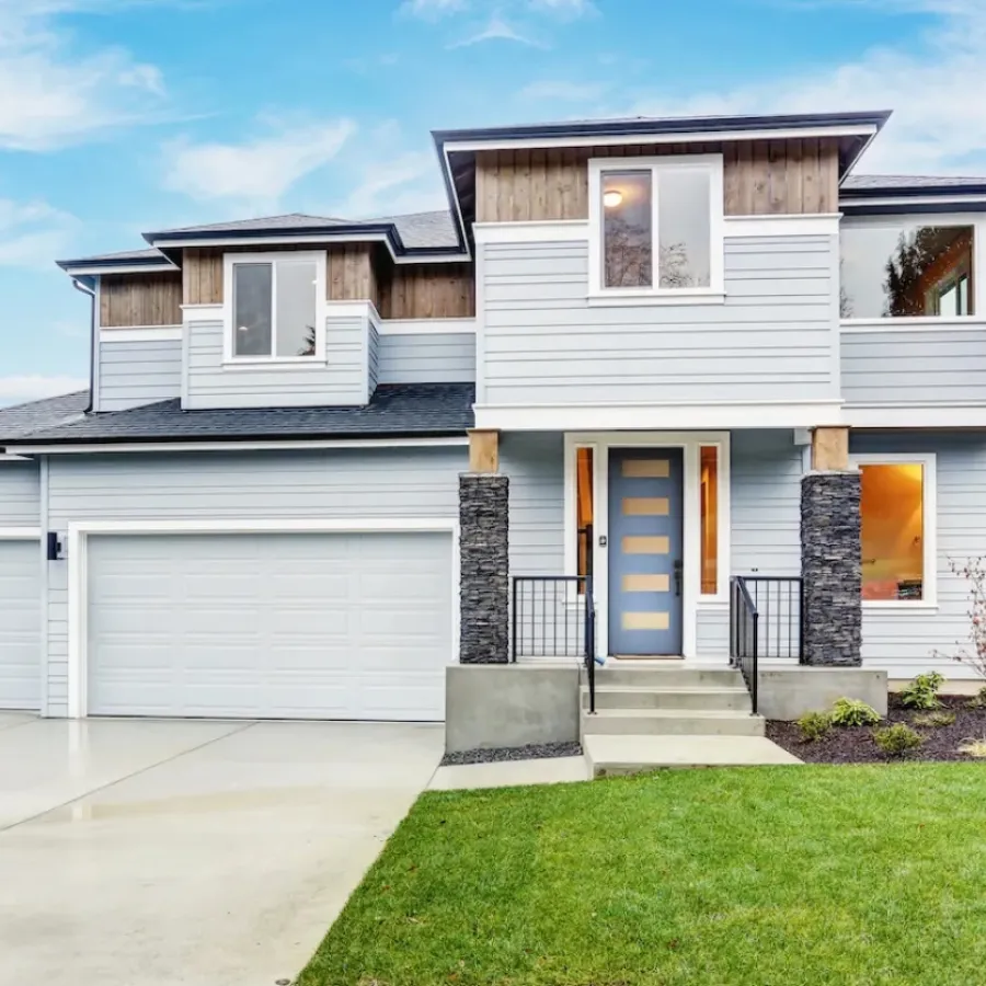 Modern two-story house with gray siding, large garage, blue front door, and well-kept lawn under blue sky.