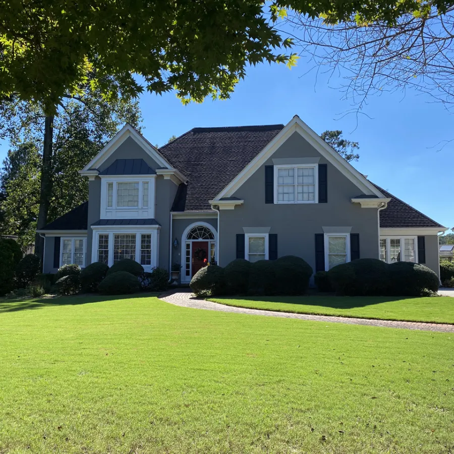 Two-story gray house with white windows, black shutters, and a large green lawn under a bright blue sky