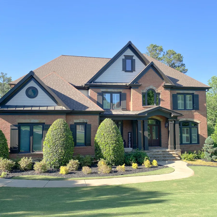 Large two-story brick house with dark shutters, and fiberglass bronze casement windows.