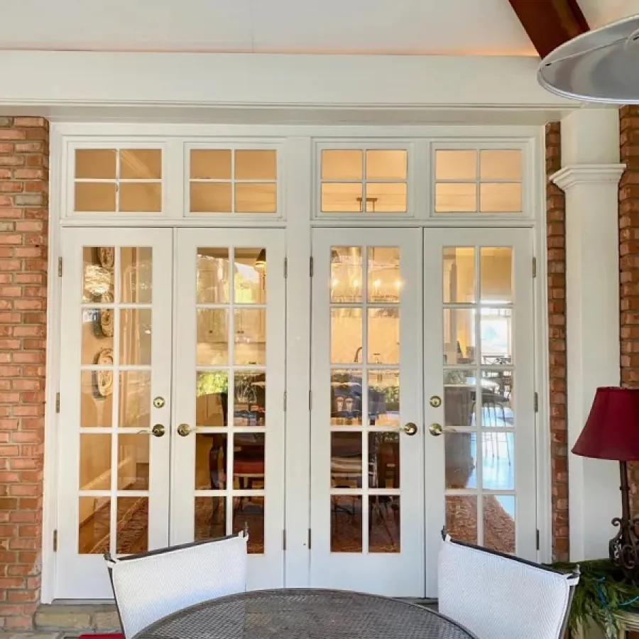 Patio with metal table and chairs in front of white French doors leading to dining room inside house.