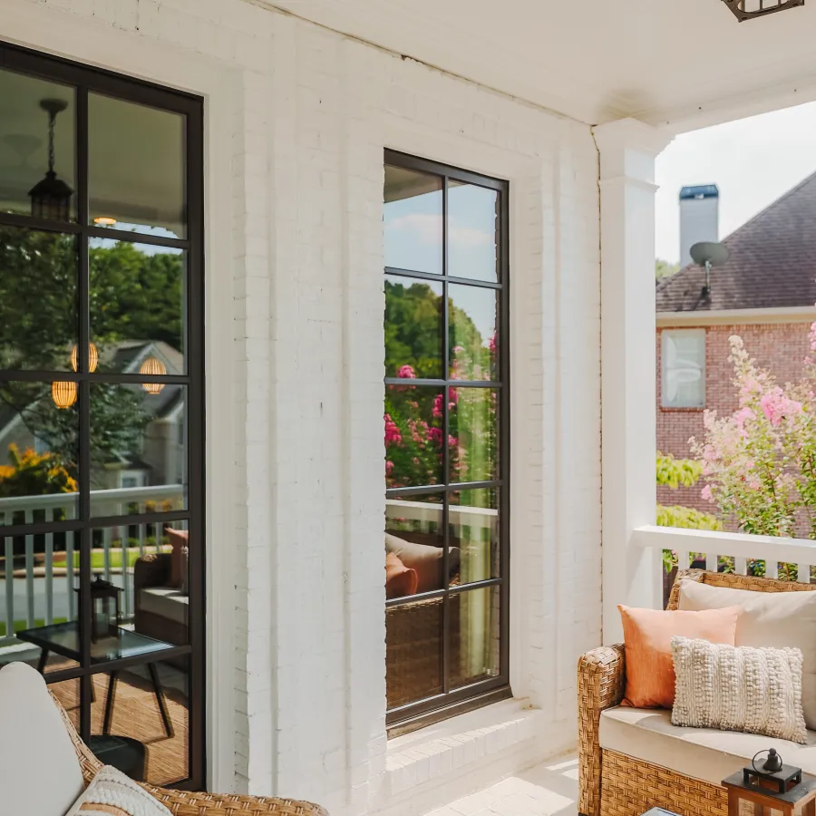 Cozy porch with wicker furniture, soft cushions, glass table, and white brick walls on a sunny day