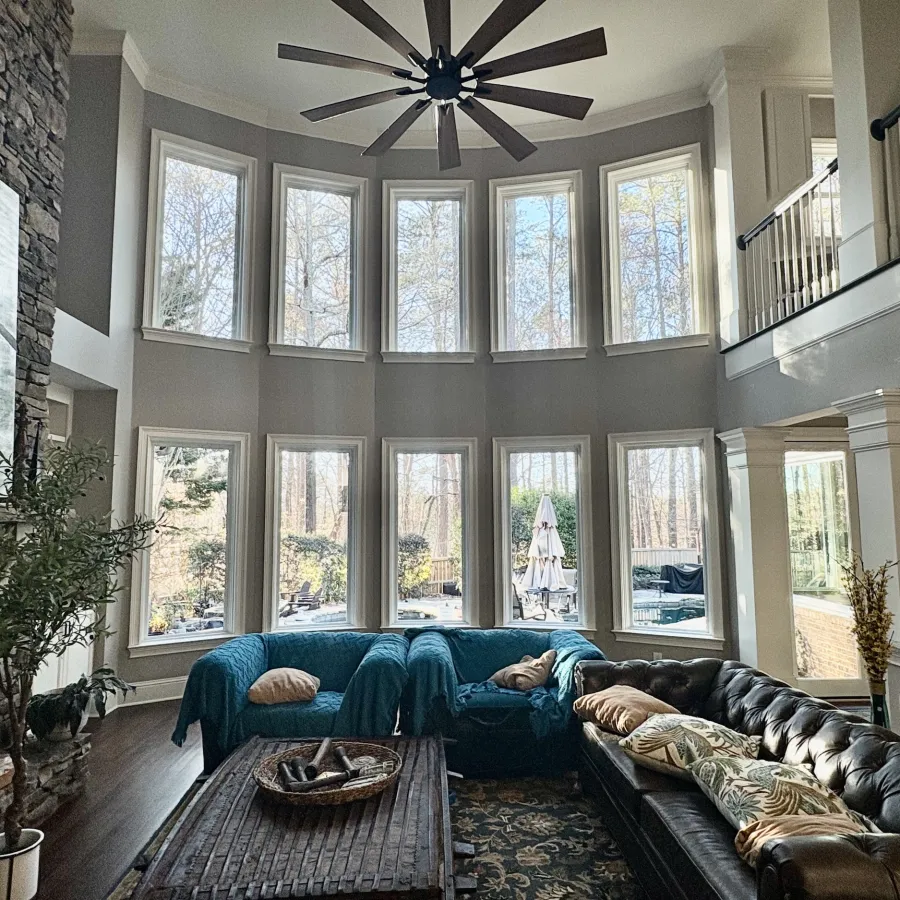 Spacious living room with tall windows, a large ceiling fan, sectional sofas, a stone fireplace, and decorative accents.